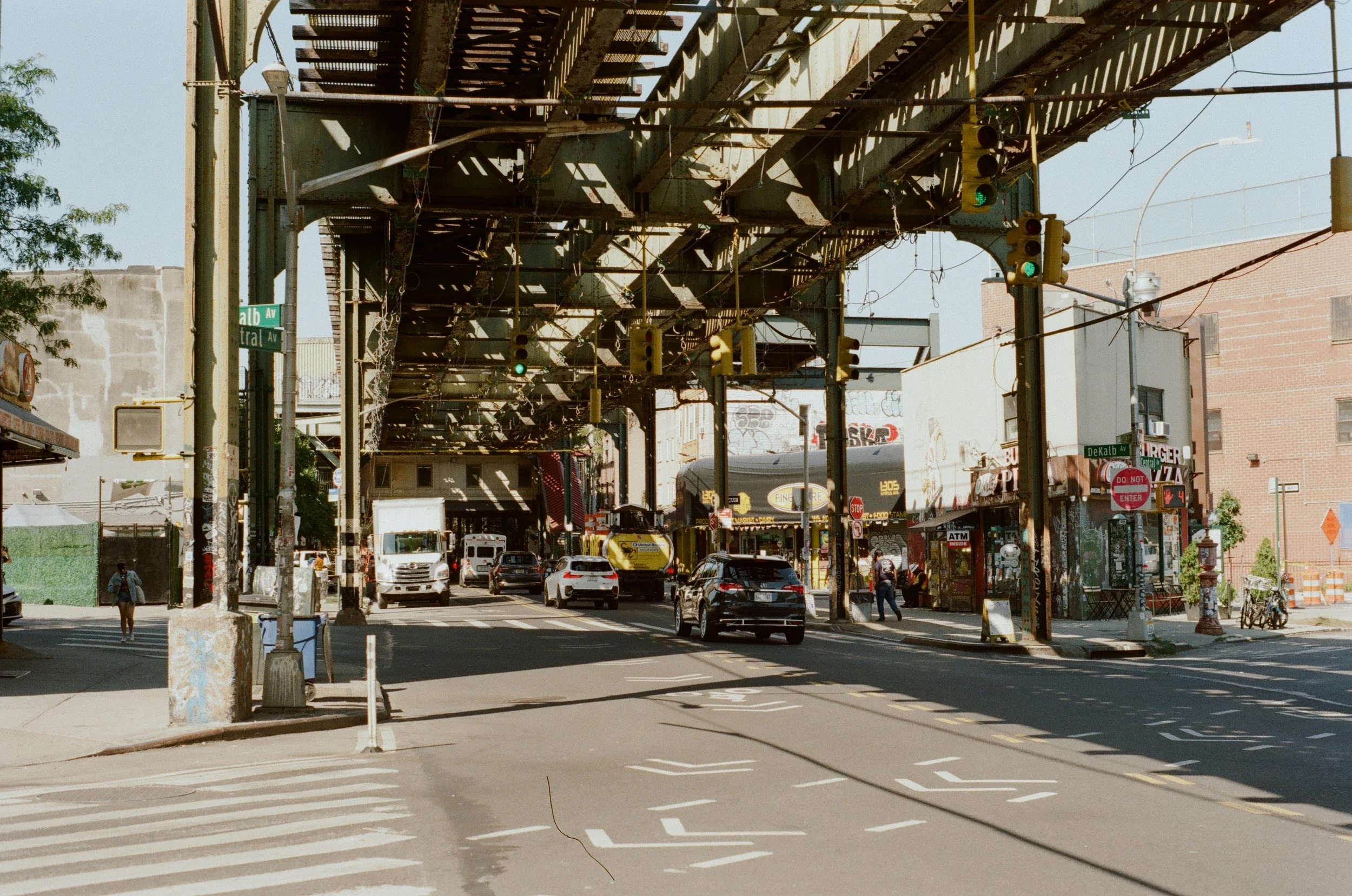 Urban street scene with elevated train tracks, cars, and buildings in the daylight.