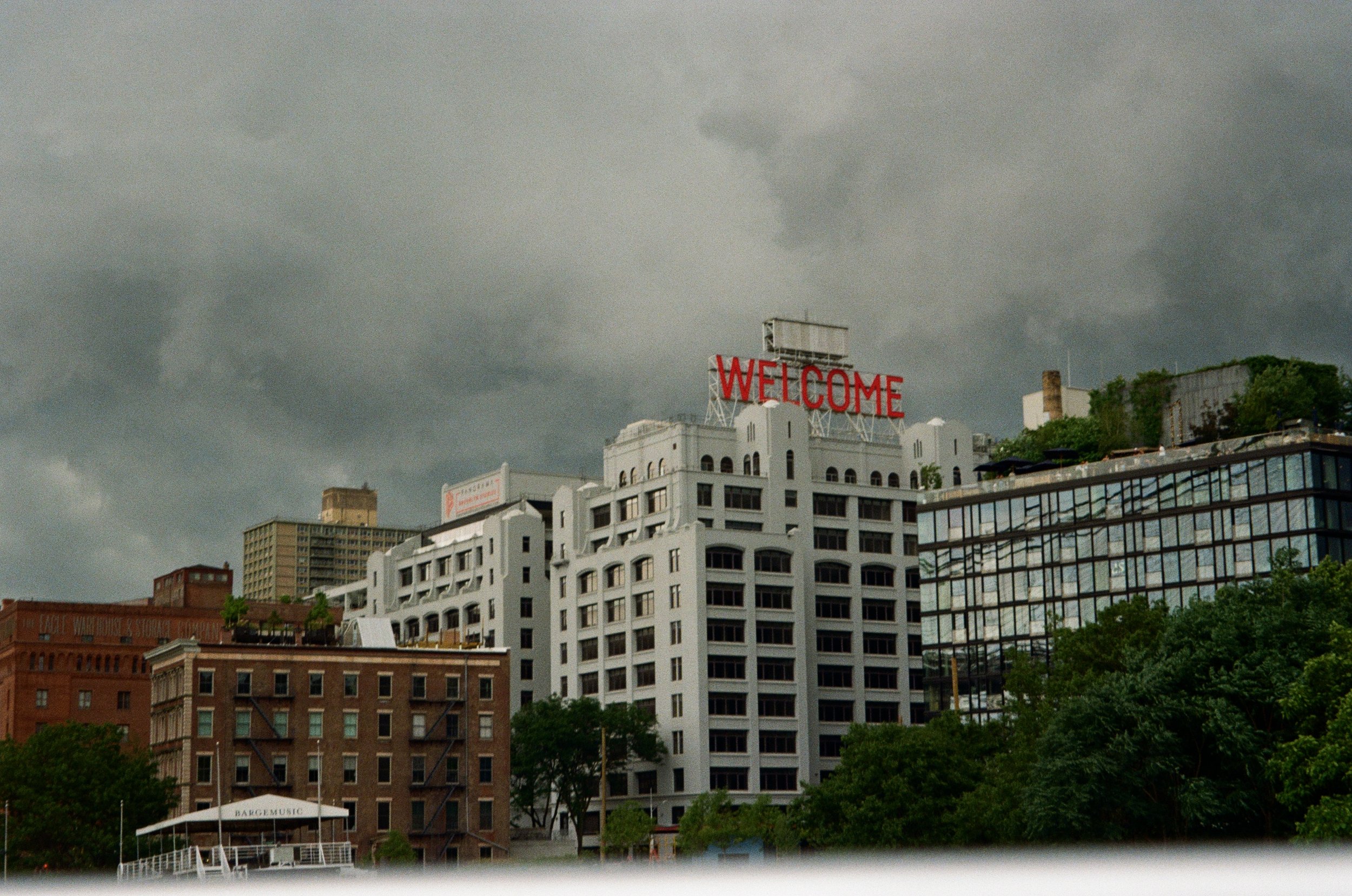 Cityscape with industrial buildings and 'Welcome' sign, under cloudy sky.