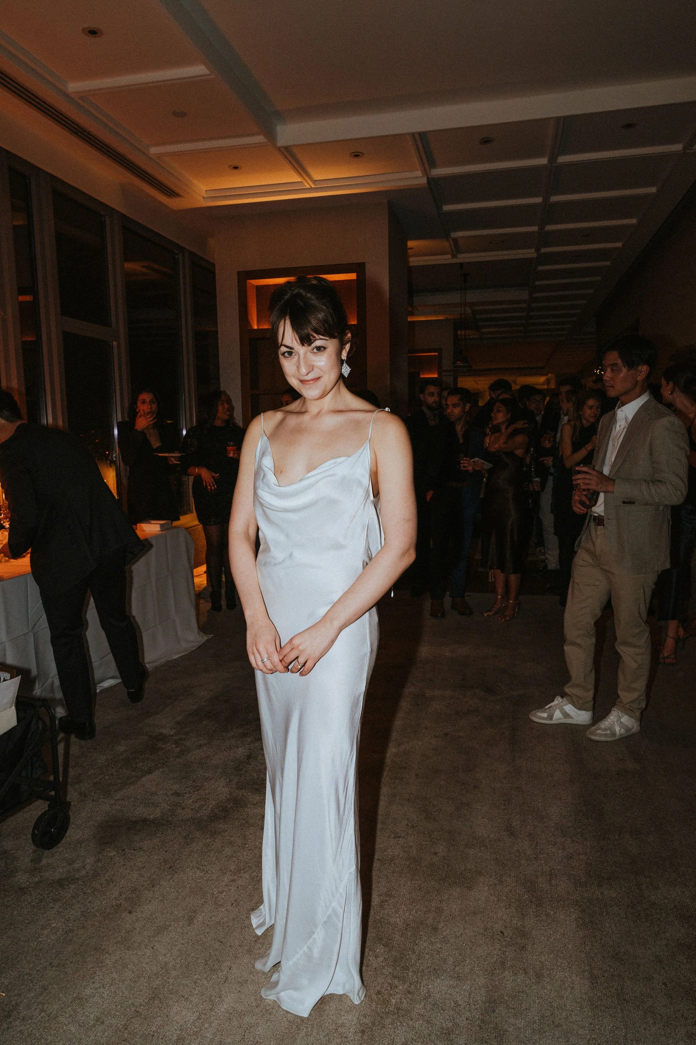 Woman in white dress at indoor party with people in background