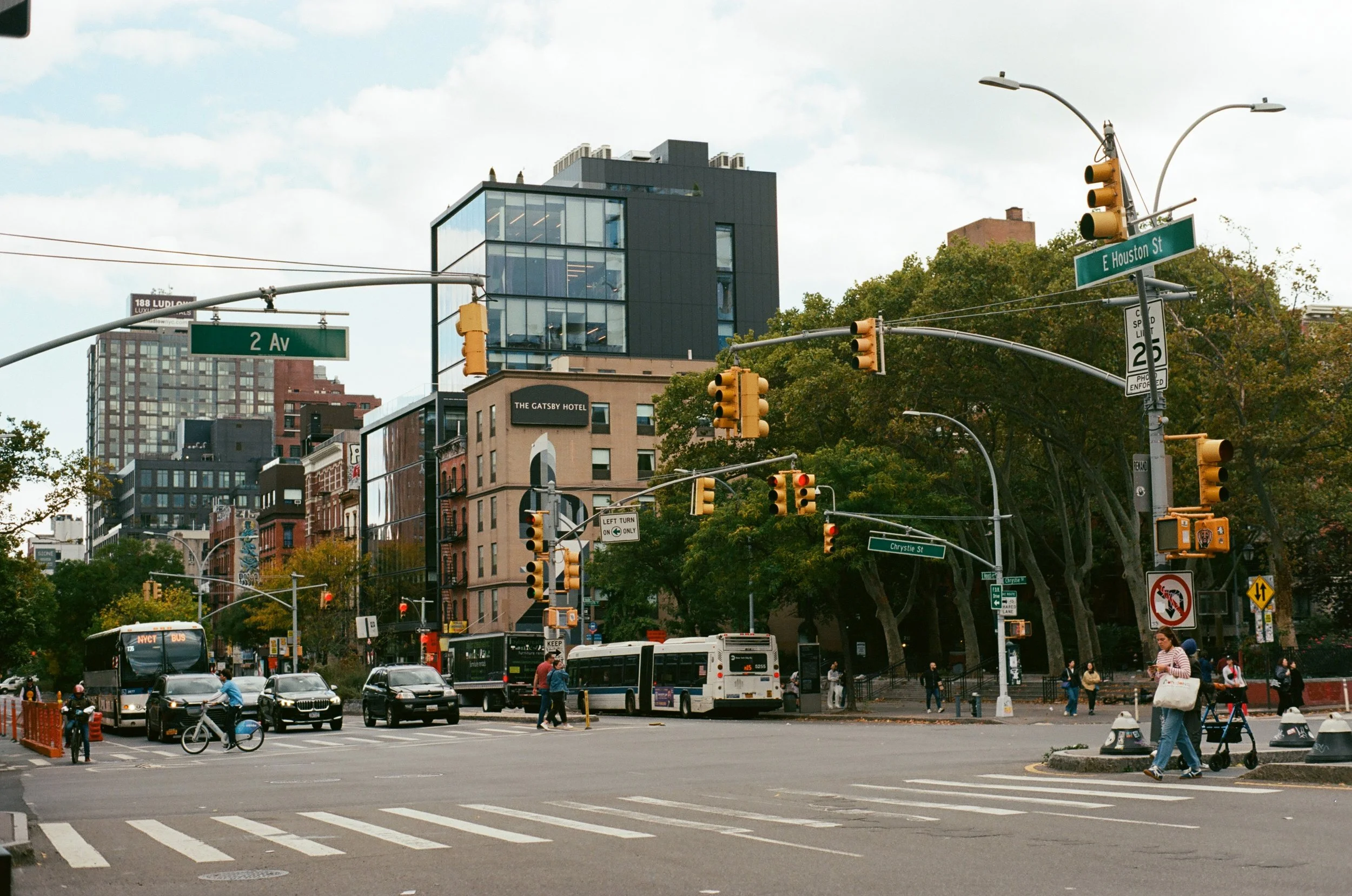 Intersection at 2nd Avenue and East Houston Street in NYC with traffic lights, cars, buses, pedestrians, and urban buildings, including The Gatsby Hotel.