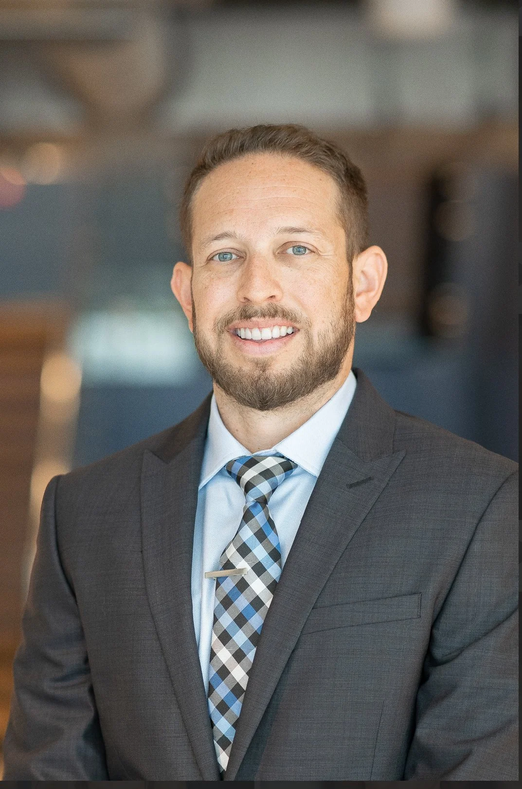 A smiling man with a beard, wearing a black athletic shirt with the letters 'ByB' and the Under Armour logo, standing against a light pink background.