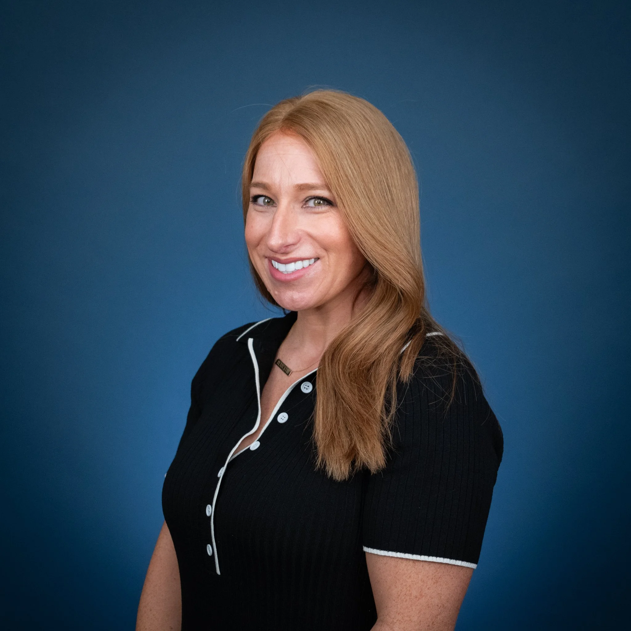 Portrait of a woman with long red hair smiling against a light blue background.
