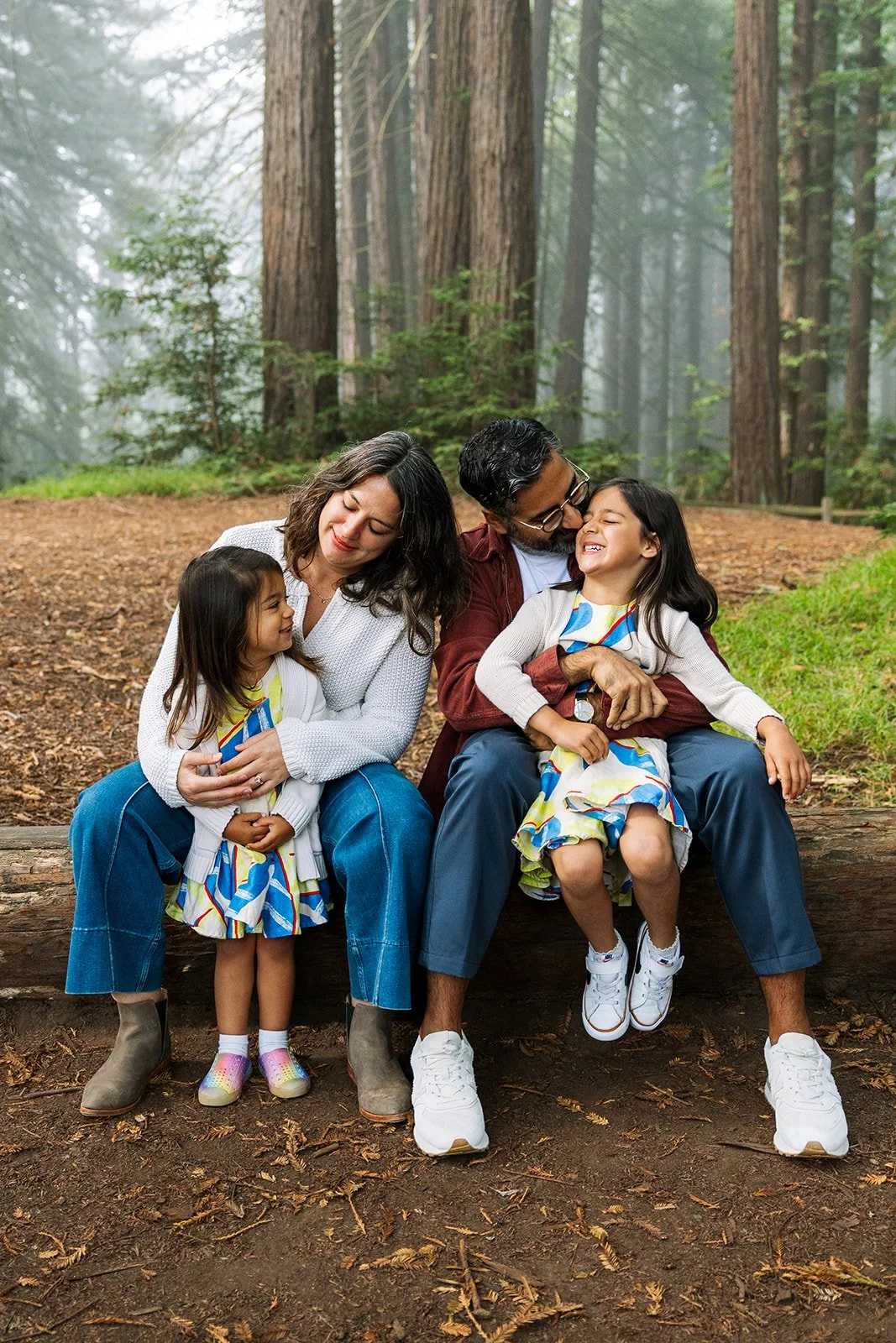 family of four sitting on a log in the oakland redwoods