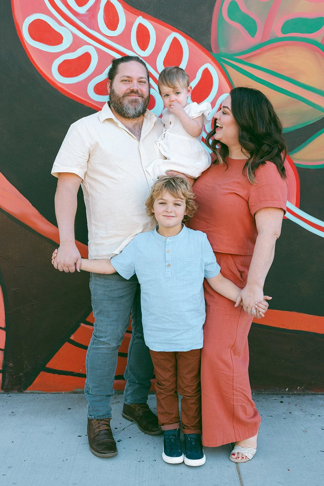 family of four standing on a sidewalk in front of a large mural