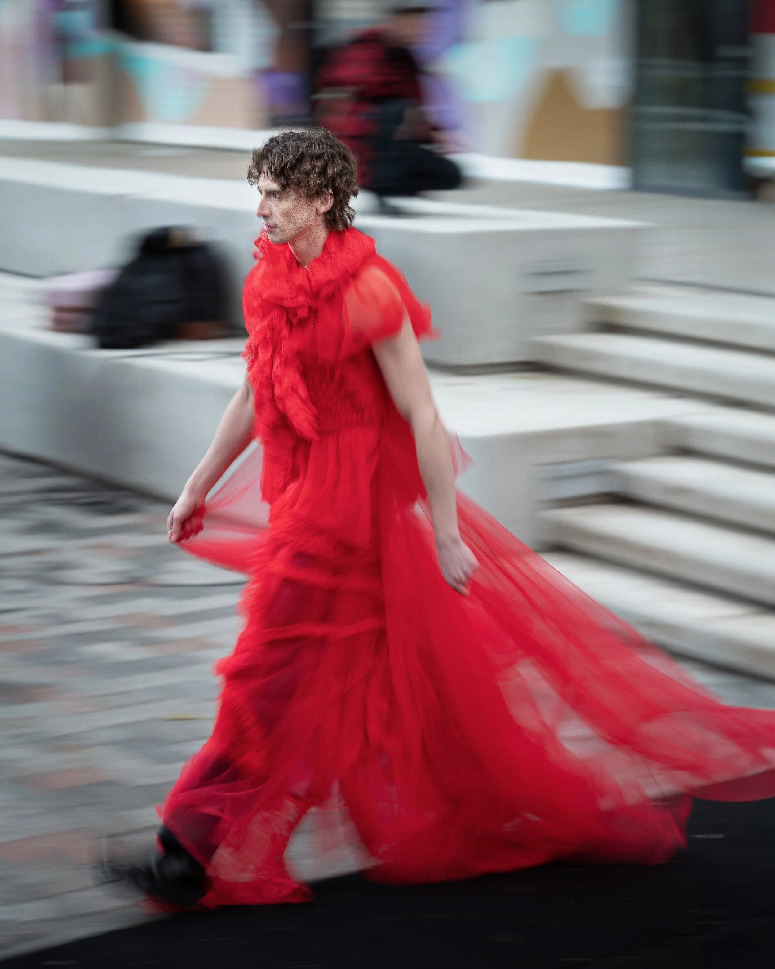A person walking outdoors wearing a flowing red dress with ruffles, with motion blur in the background.