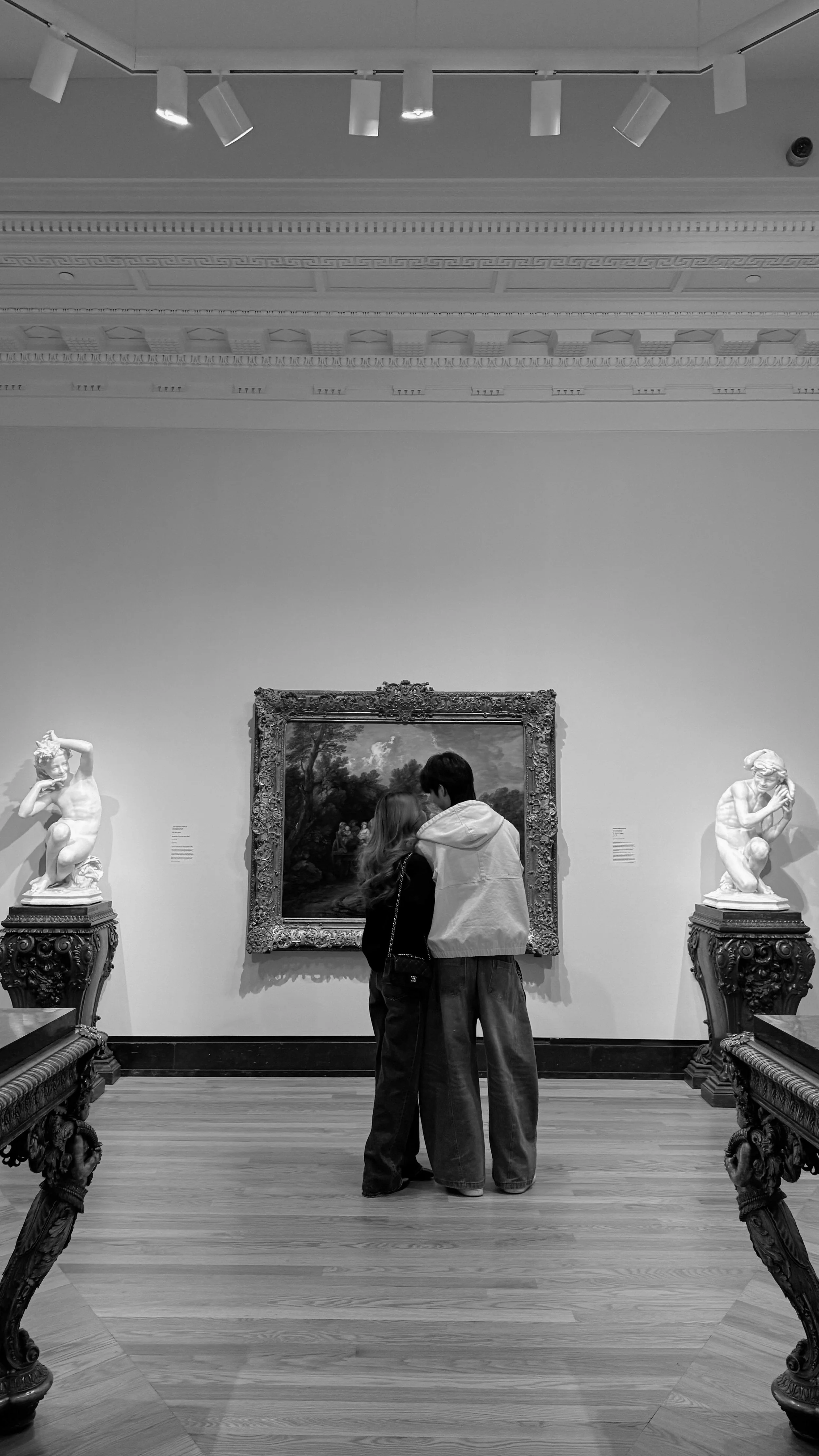 Two people in front of a painting in an art museum, surrounded by classical sculptures on pedestals.