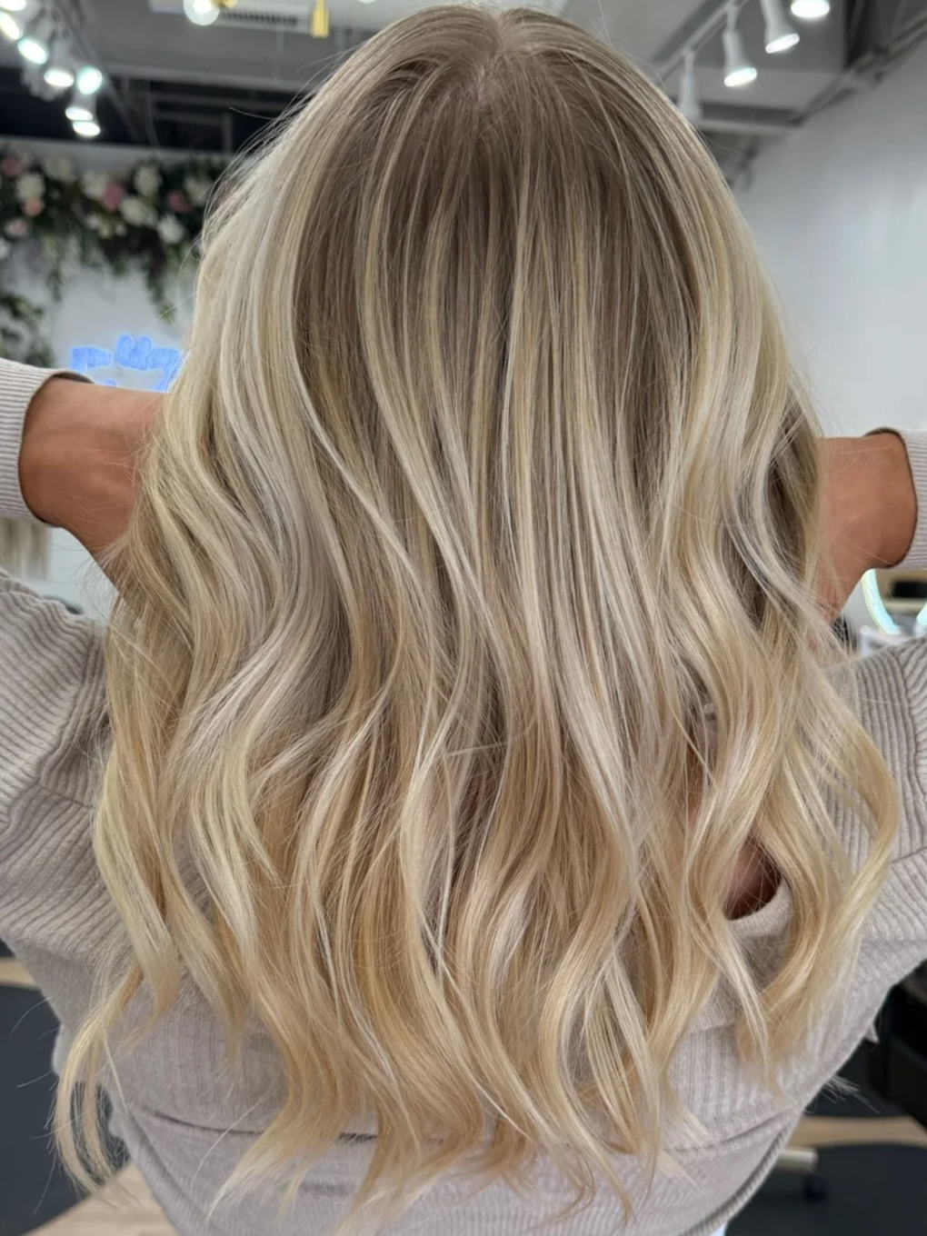 Close-up of a woman with wavy, shoulder-length blonde hair, slightly turned to the side, in an indoor setting.