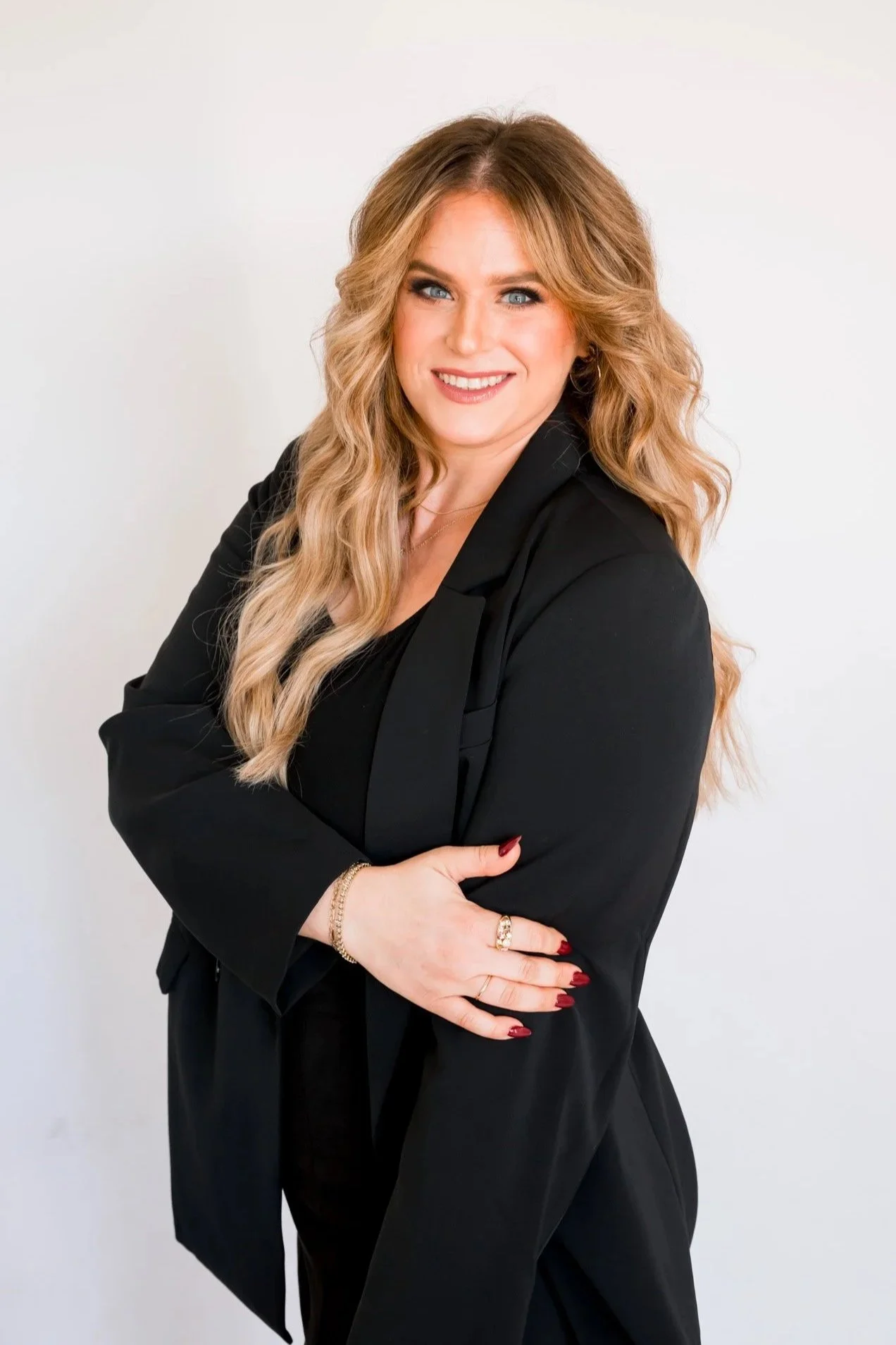 A woman smiling wearing a black blazer, she is a hairstylist with long blond hair