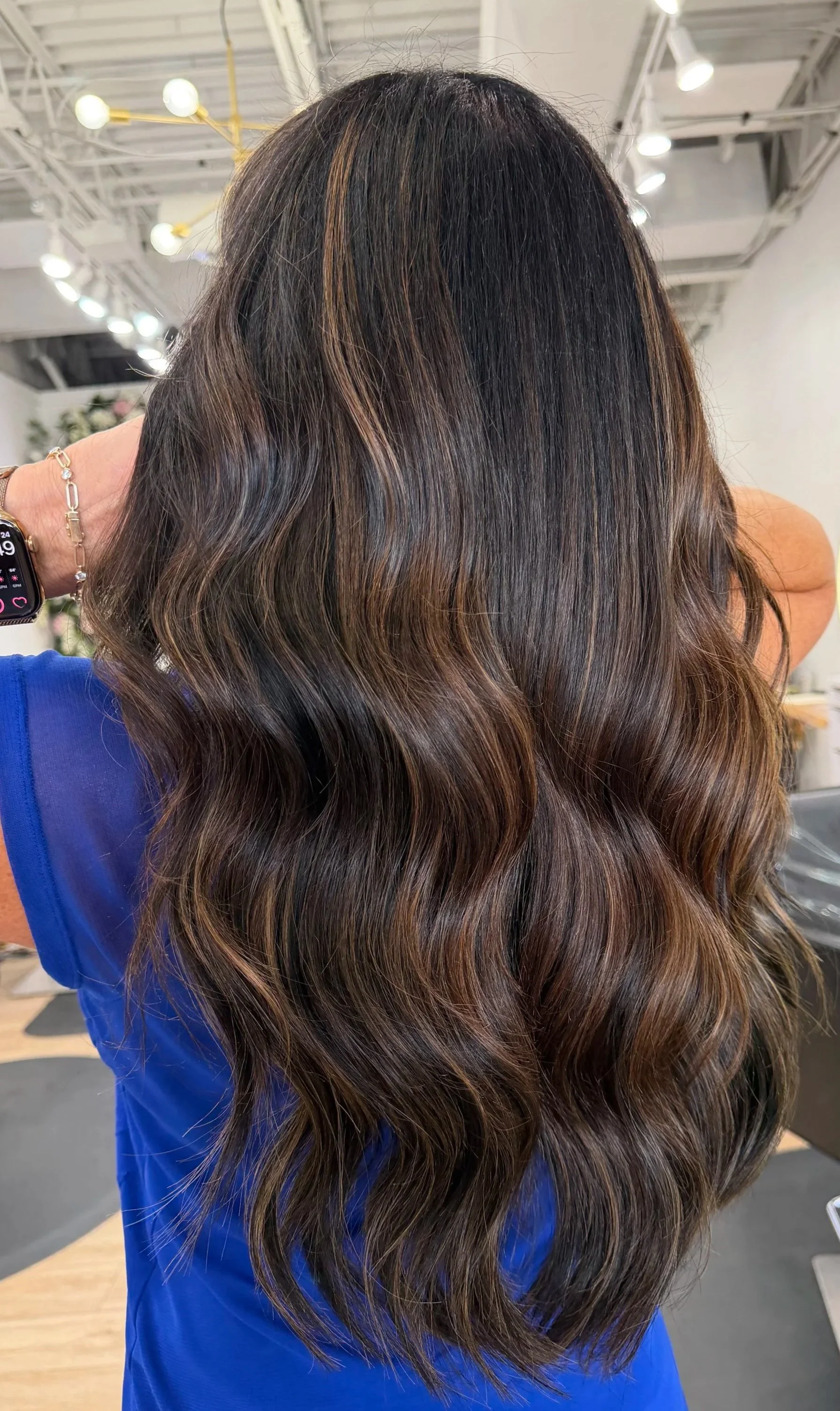 Back view of a woman with long, wavy blonde hair wearing a red sweater inside a store or salon.