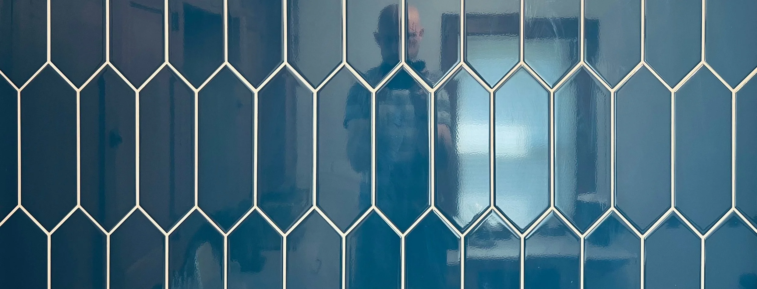 Close-up of a blue tile wall with a geometric pattern of light grout lines forming diamond shapes.