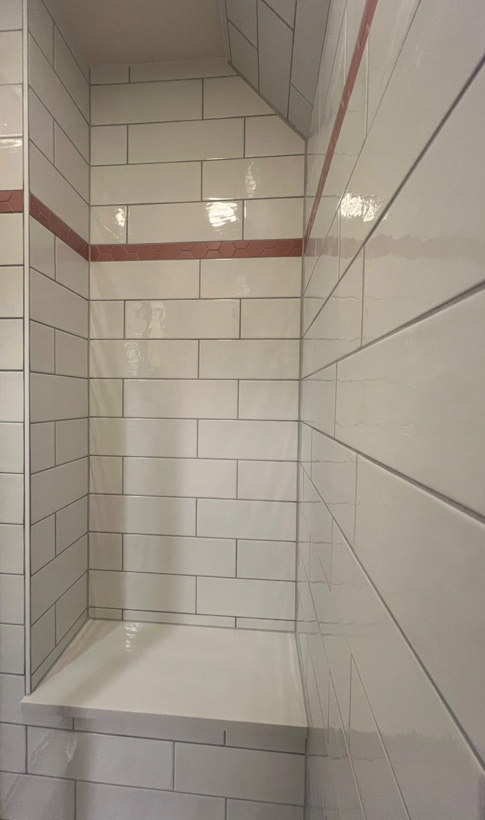 Empty tiled shower with white rectangular tiles and a horizontal strip of red hexagonal tiles.