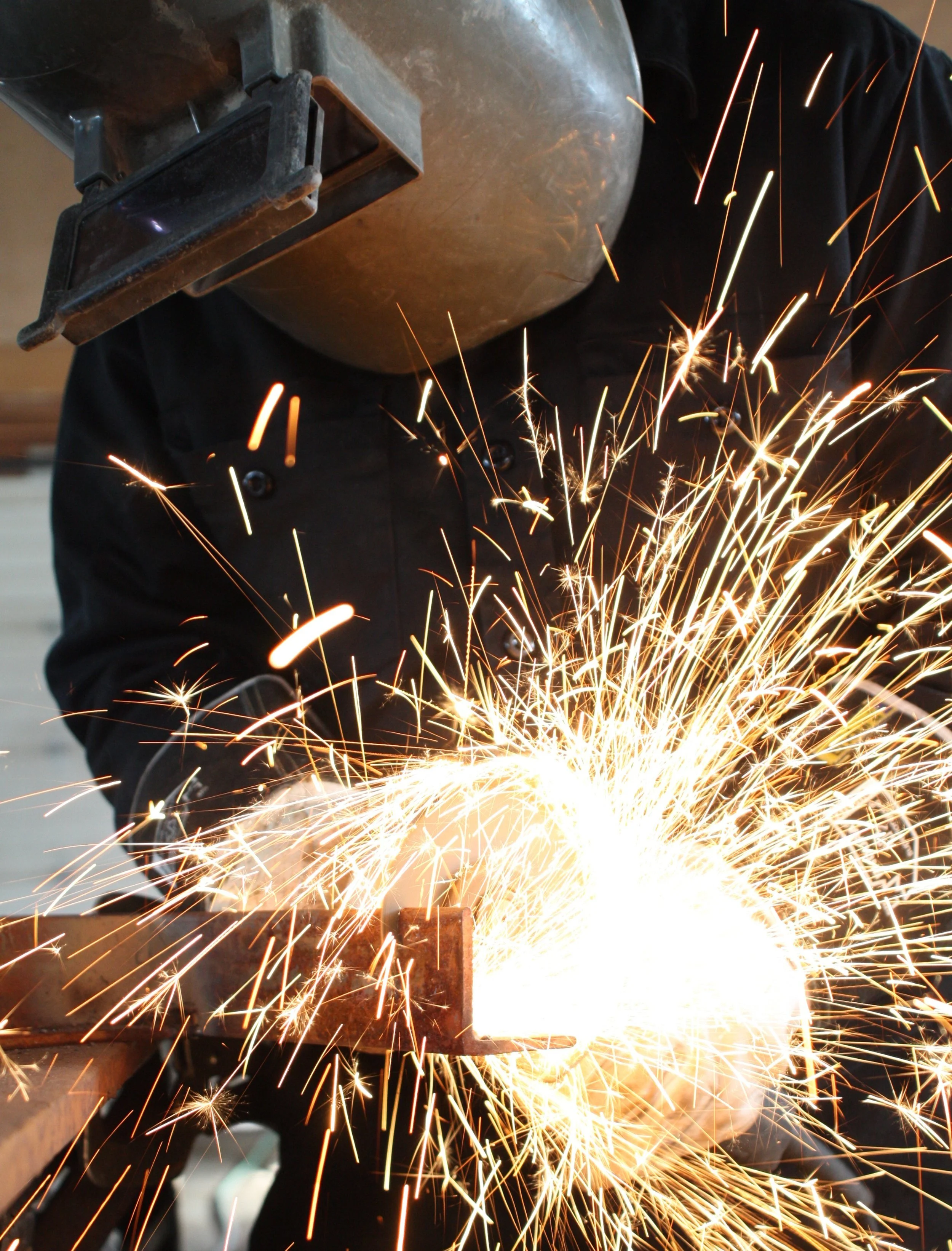 Un soudeur en train de souder un métal, produisant des étincelles brillantes dans un atelier.