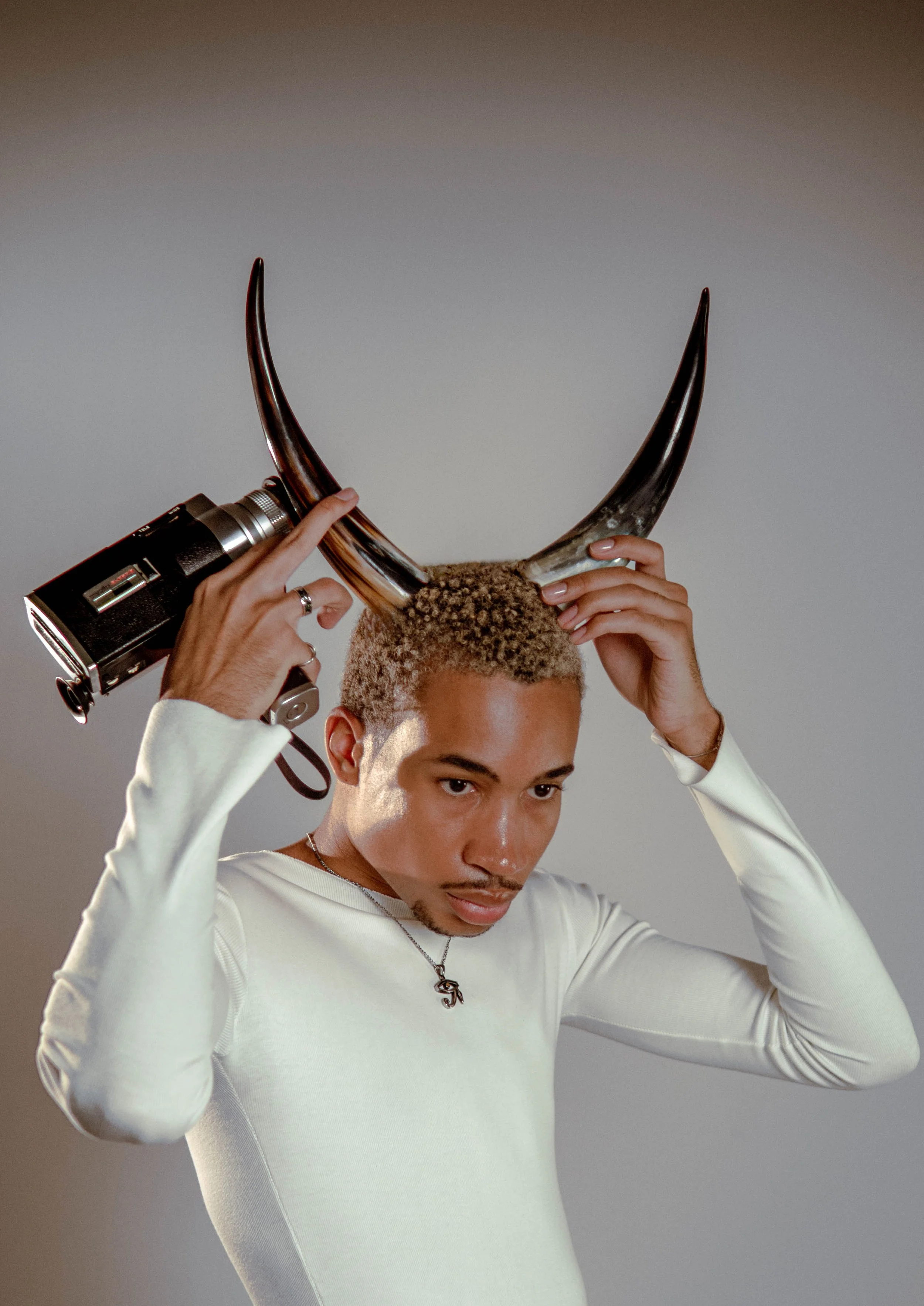Young man holding a vintage camera to his head and wearing antler-shaped headphones.