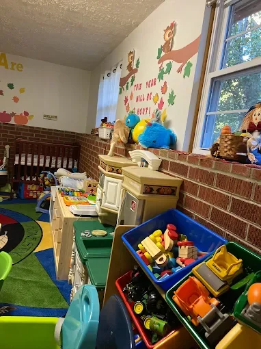A colorful children's classroom corner with toys, a play kitchen, and a painted wall with hands and autumn leaves.