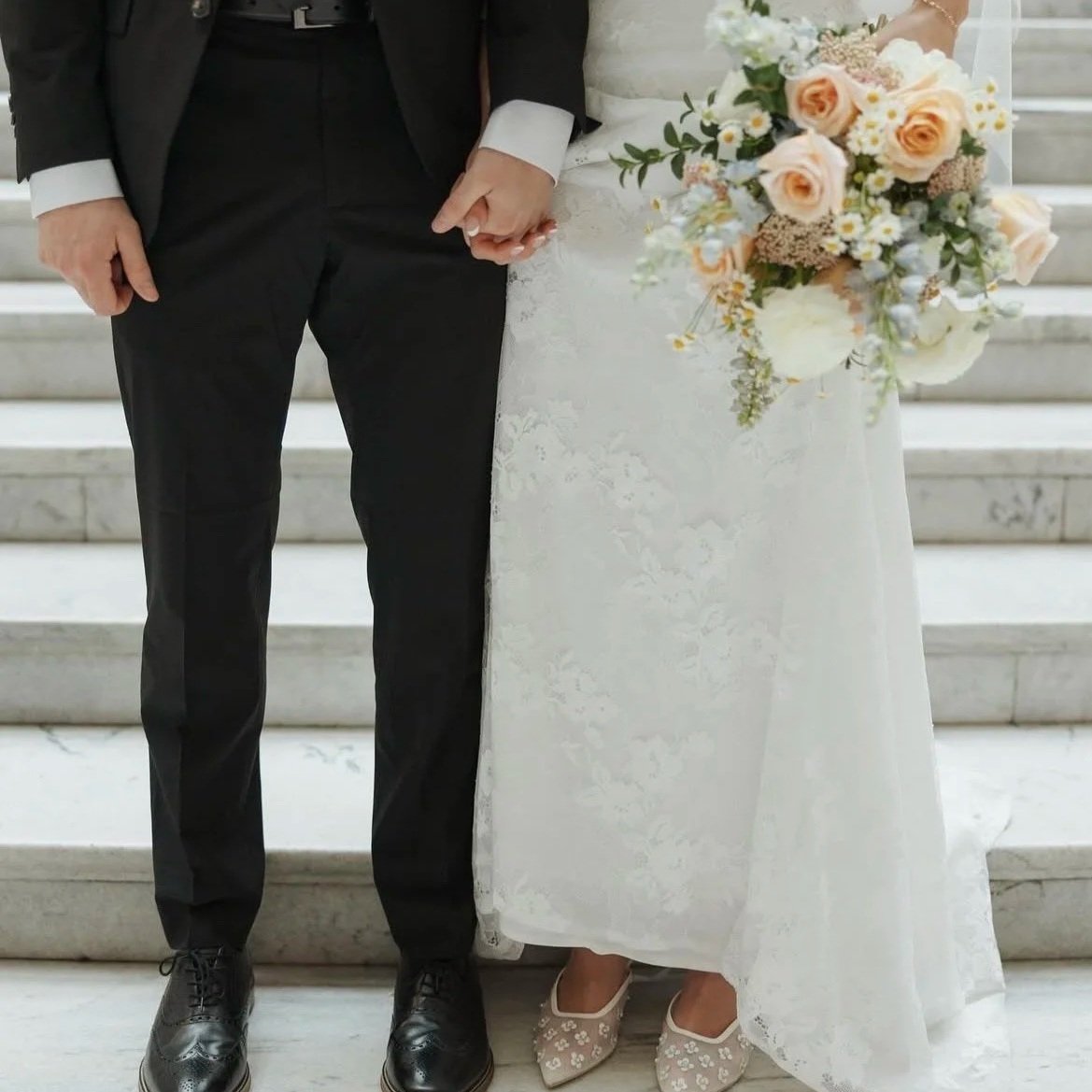 A bride and groom holding hands on stairs. The bride is holding a bouquet of flowers from a McKinney, Texas florist.