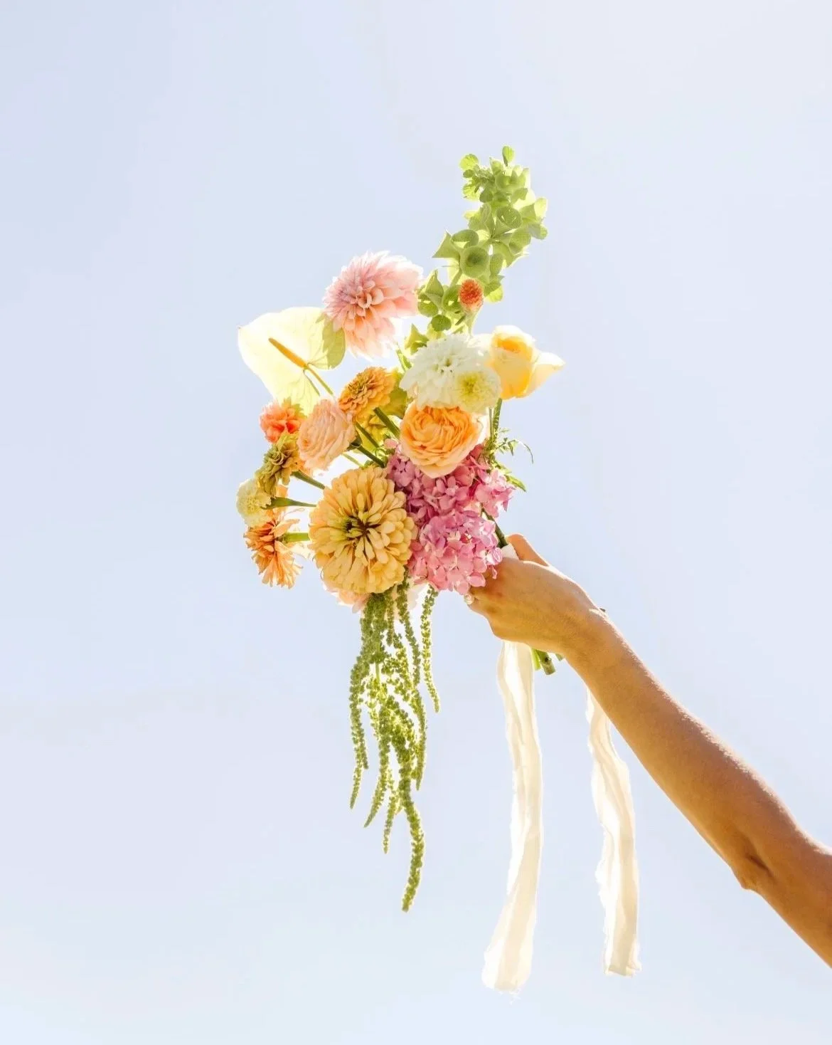 Hand holding a bouquet of colorful flowers against a light sky background in McKinney, Texas.
