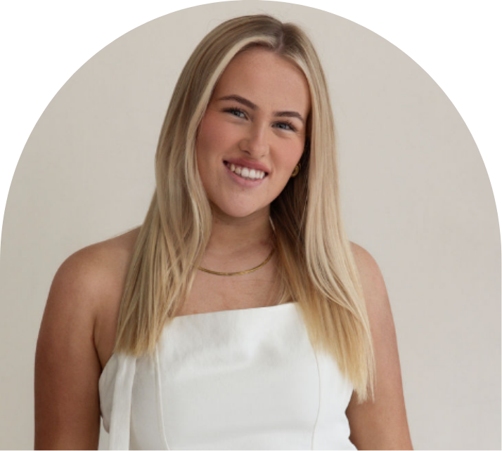 A young woman with long blonde hair, wearing a white strapless top and gold jewelry, smiling at the camera.