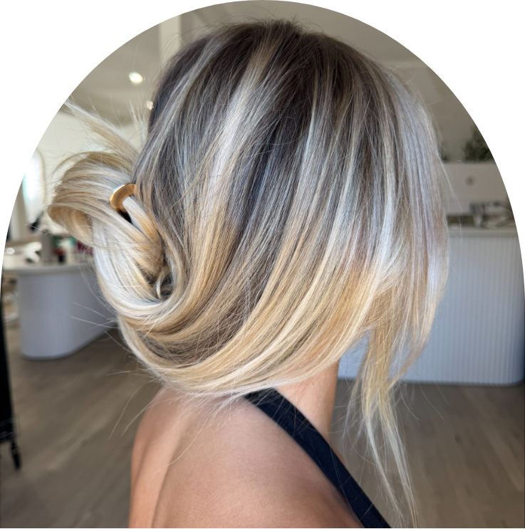 Woman with shoulder-length blonde hair styled in a loose updo, sitting indoors near a white counter or reception area.