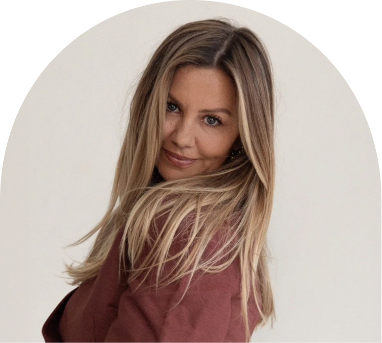 A woman with long blonde hair, wearing a maroon blazer, looking at the camera and smiling against a plain white background.