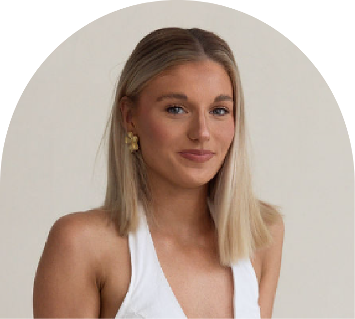 A young woman with shoulder-length blonde hair wearing a white sleeveless top and gold earrings, smiling slightly, standing against a plain white background.