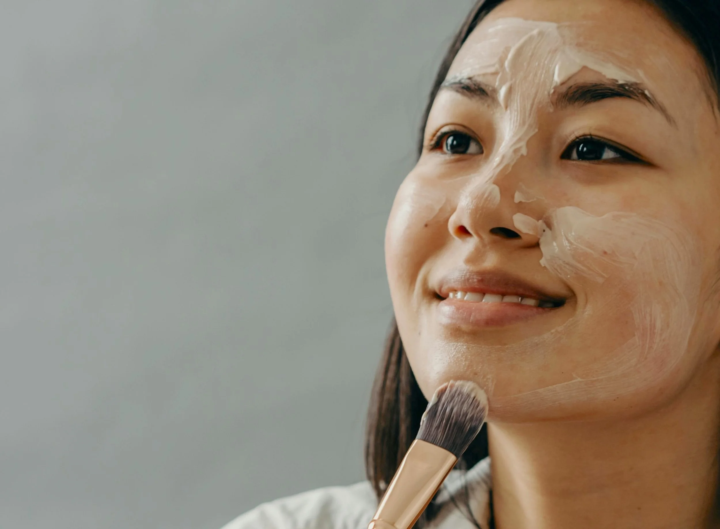 A woman applying a facial mask with a brush.