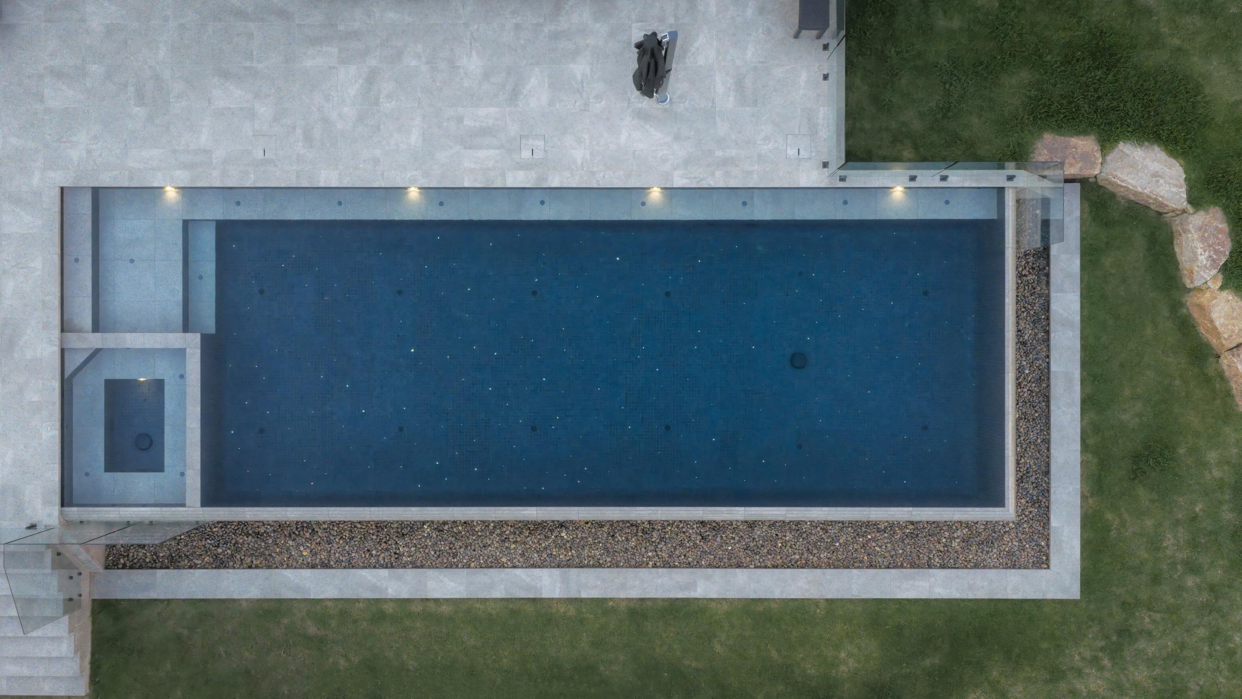Aerial view of a wet-edge swimming pool with starlight-inspired lighting illuminating the water from within.