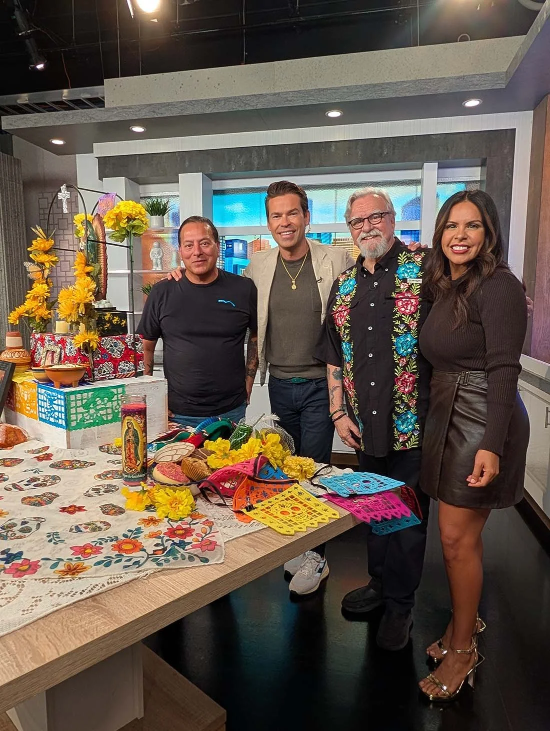 MECA Houston representatives and media personalities smiling together on a TV studio set decorated with a Día de los Muertos ofrenda and marigolds, featuring earned media coverage secured through Houston nonprofit PR campaign