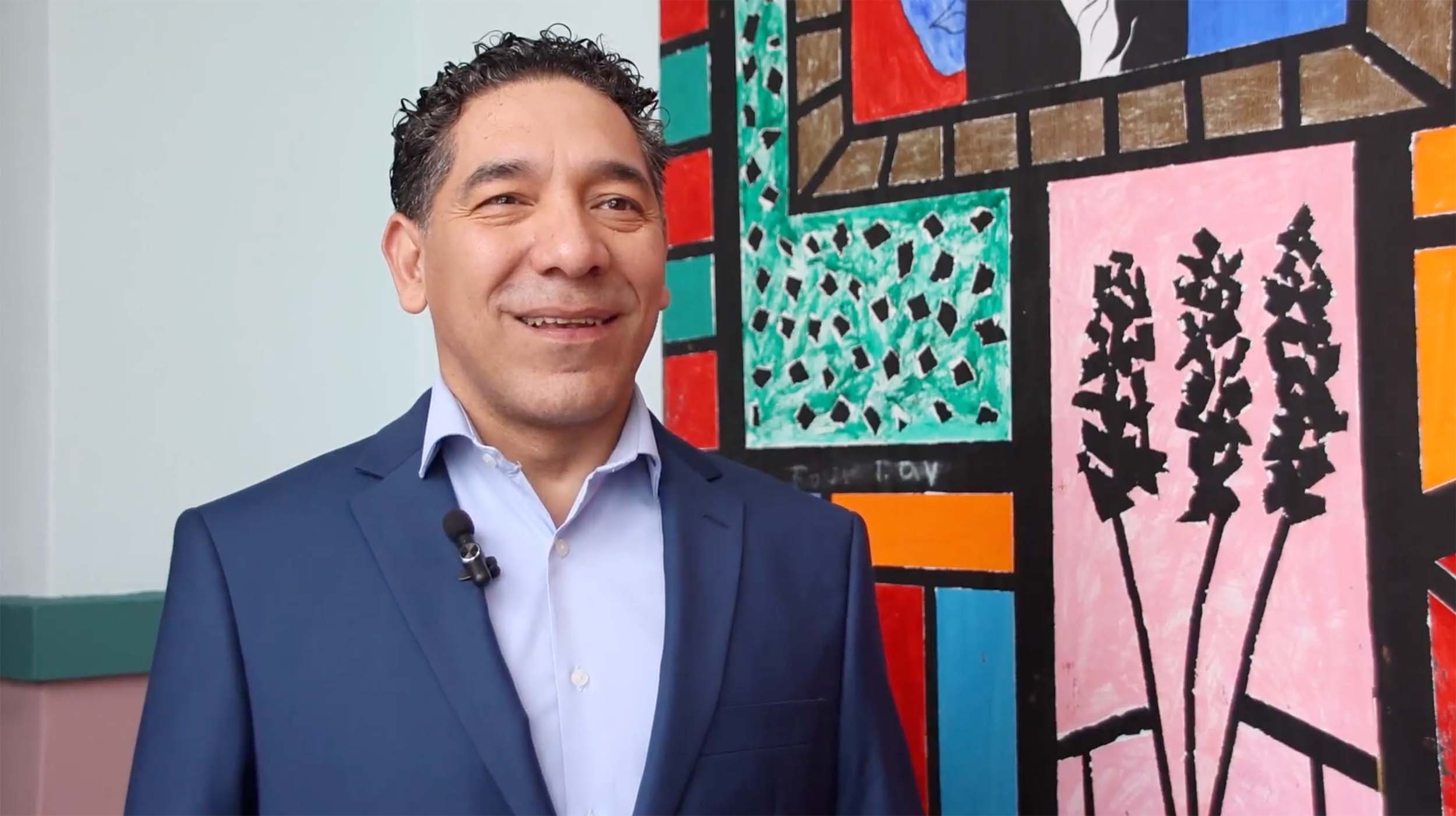 Smiling male executive in a navy suit with a lapel microphone standing in front of a colorful mural, positioned as a trusted thought leader through Houston executive PR strategy
