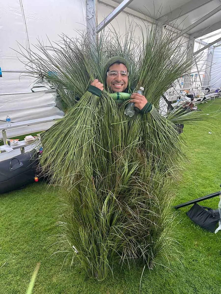 Erik "Bush B79" Solorzano, 2026 Benito Bowl performer, smiling playfully while dressed in a full grass bush costume at the Super Bowl