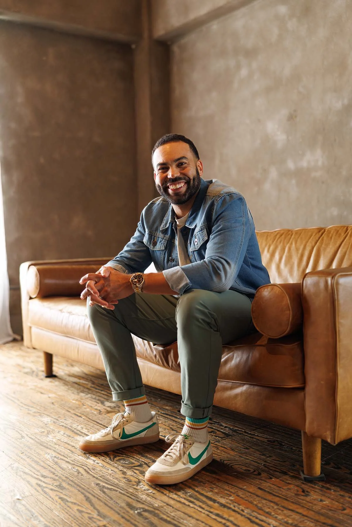 Terry Williams, author, mindset coach, and TEDx speaker, smiling confidently while seated on a leather couch in a relaxed editorial portrait