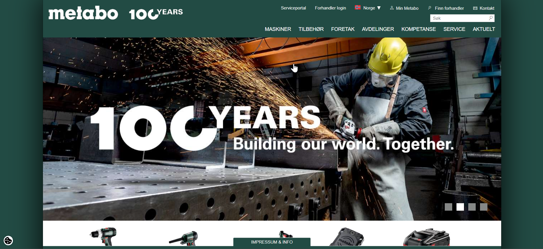 En person iført verneutstyr som skjerm, hjelm og hansker bruker en elektrisk sirkelsag eller vinkelsag på metall i en industrihall. Det er gnister som flyr fra sagkuttet.