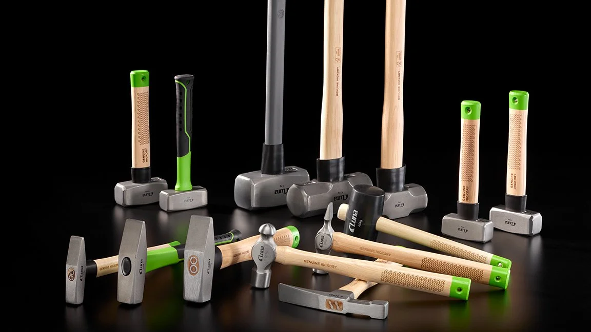 Diverse hammere og meisler på en svart bakgrunn, inkludert flere hammere med ulike gripe- og hovedyper, og noen meisler av tre og metall.