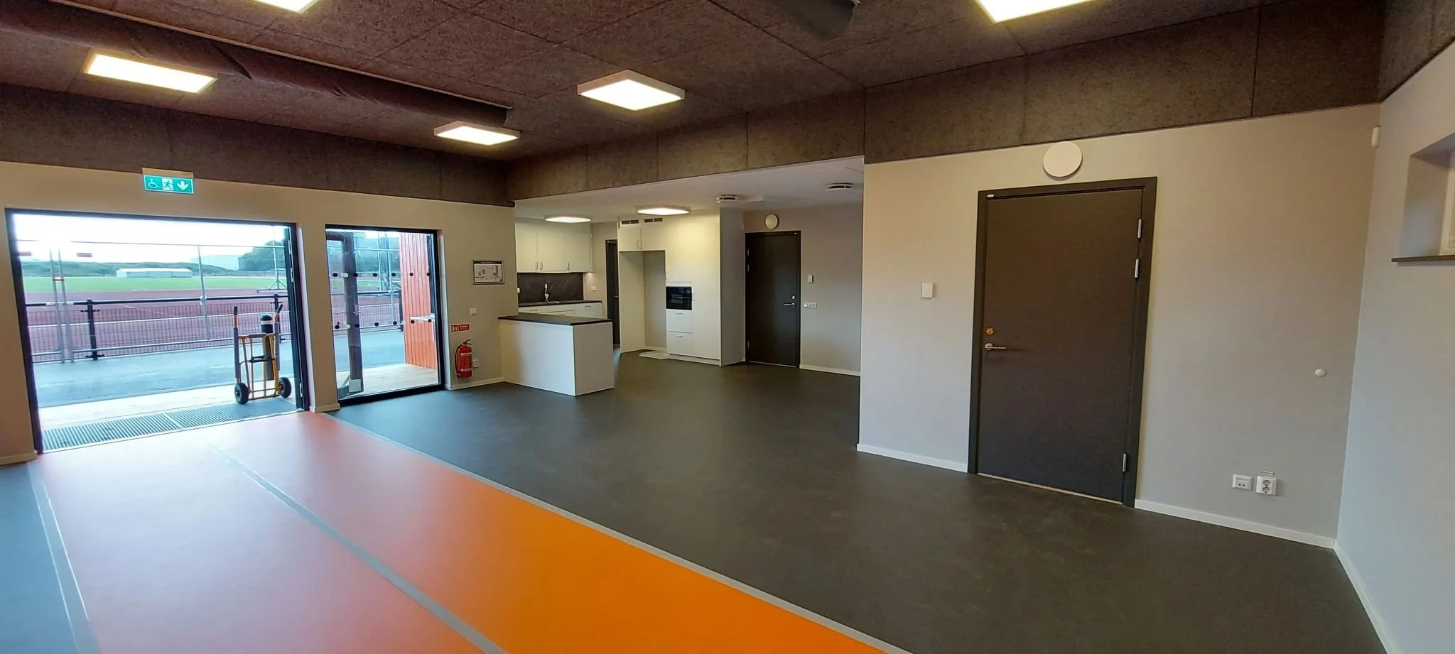 Interiör av klubbstuga med mörkt tak, mörkgrå dörrar och oranget golv.