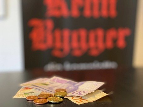 Ett antal mynt och sedlar på en svart yta med en mörk bakgrund där man ser Rehn Byggers röda logtoyp.