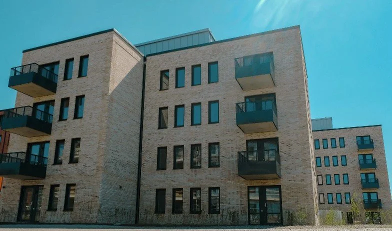 Moderna flerfamiljshus med ljus tegel och svarta balkonger under en klar blå himmel.