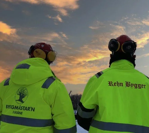 Två varseljackor med Byggmästar’n i Skåne och Rehn Bygger logotyper – symbol för företagets samarbete och arbetsmiljö.