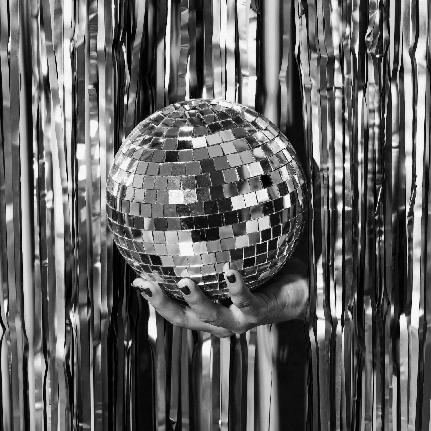 A person holding a disco ball in front of metallic streamers background.