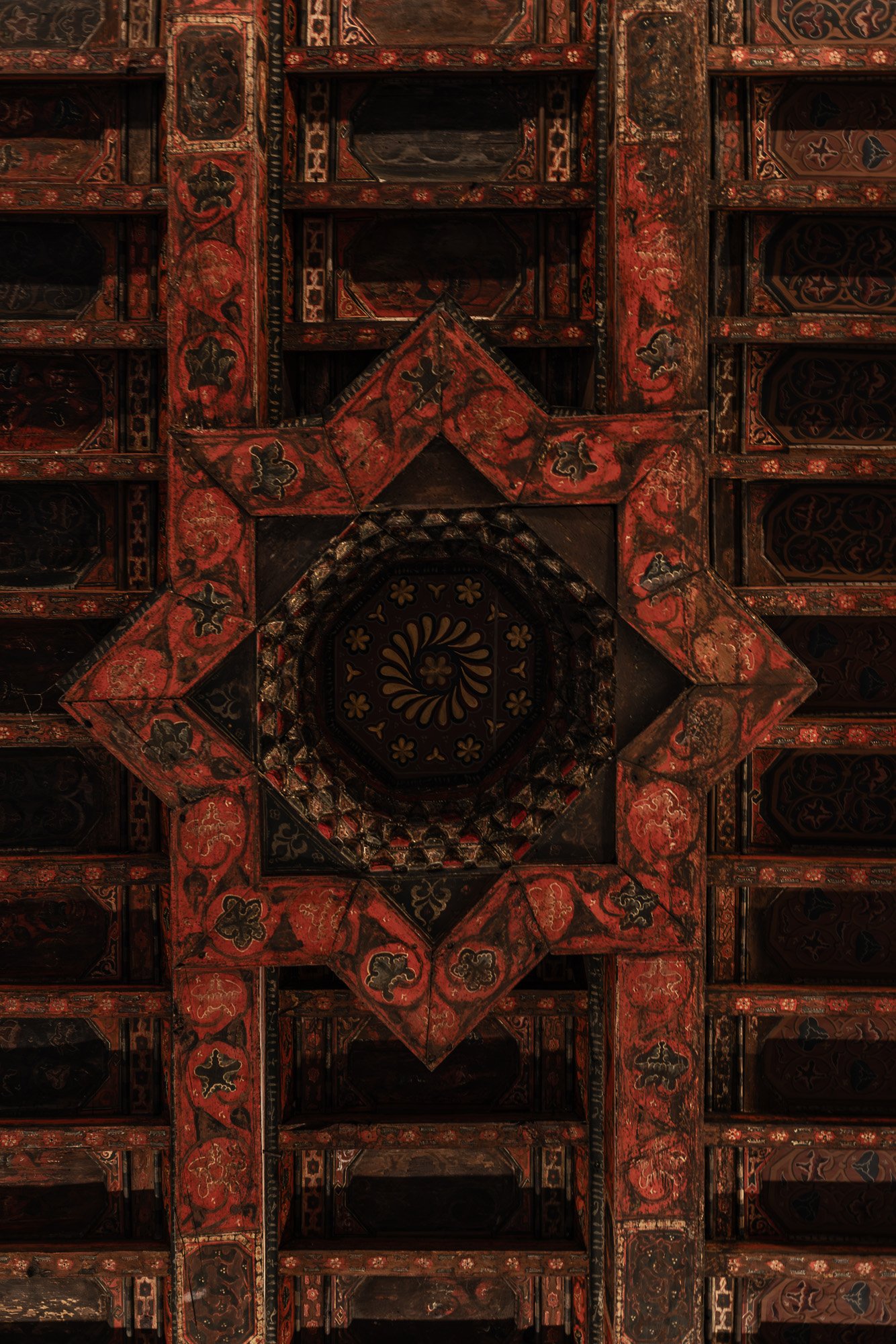 Close-up of an intricately painted red and black wooden ceiling with geometric patterns and floral motifs.