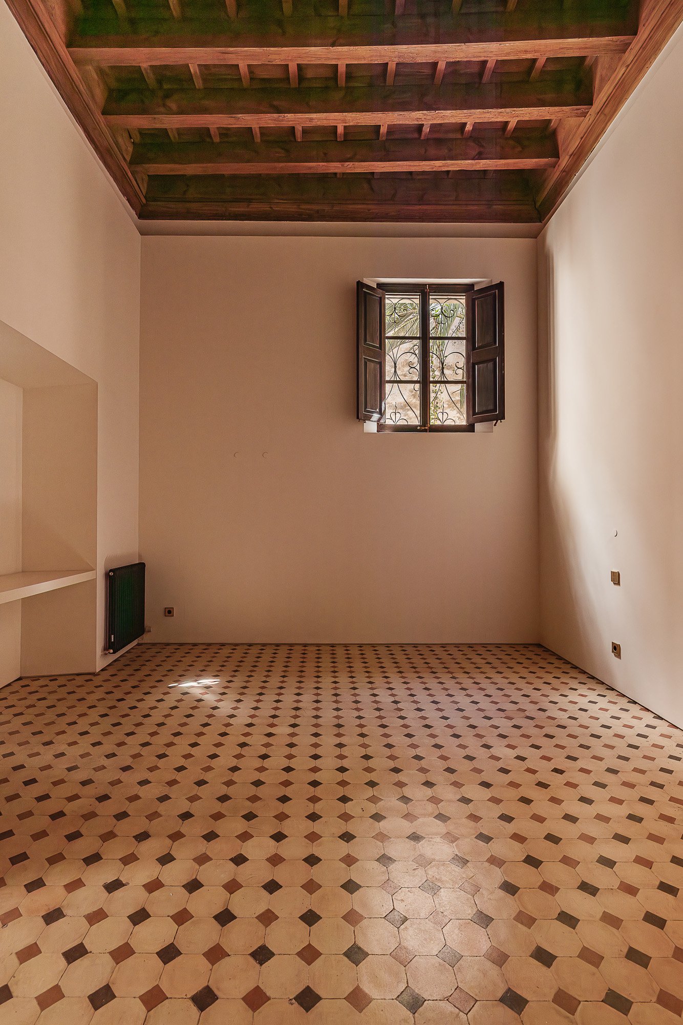 Empty room with tiled floor, white walls, a small window with open wooden shutters, and a wooden ceiling.
