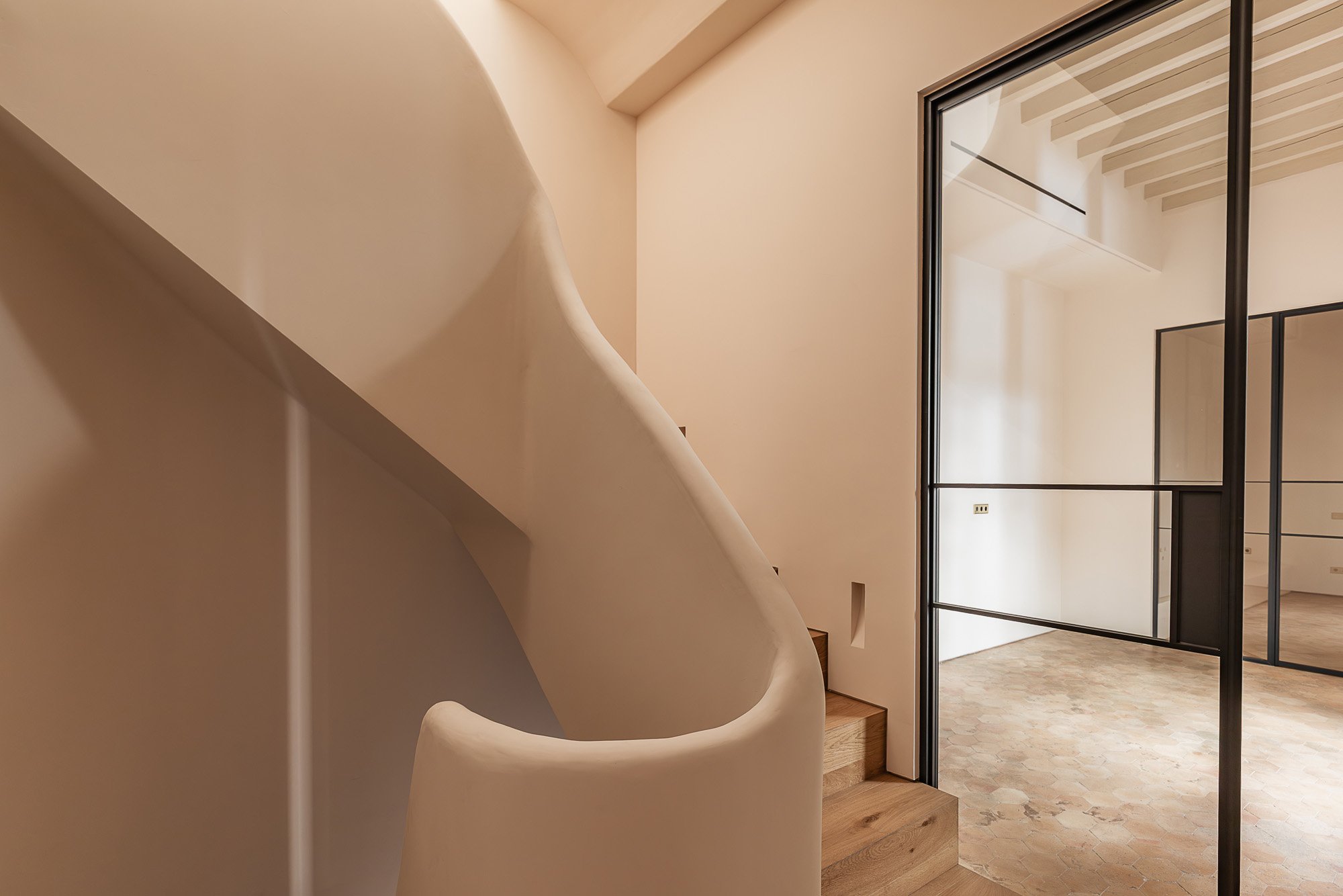 Modern interior with a curved staircase, wooden steps, and a large glass door leading to a room with a hexagonal tile floor.