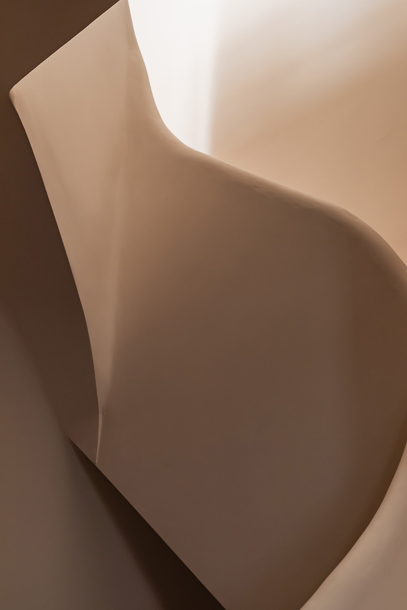 Close-up view of a smooth, beige-colored abstract sculpture or paper with gentle curves and shadows.