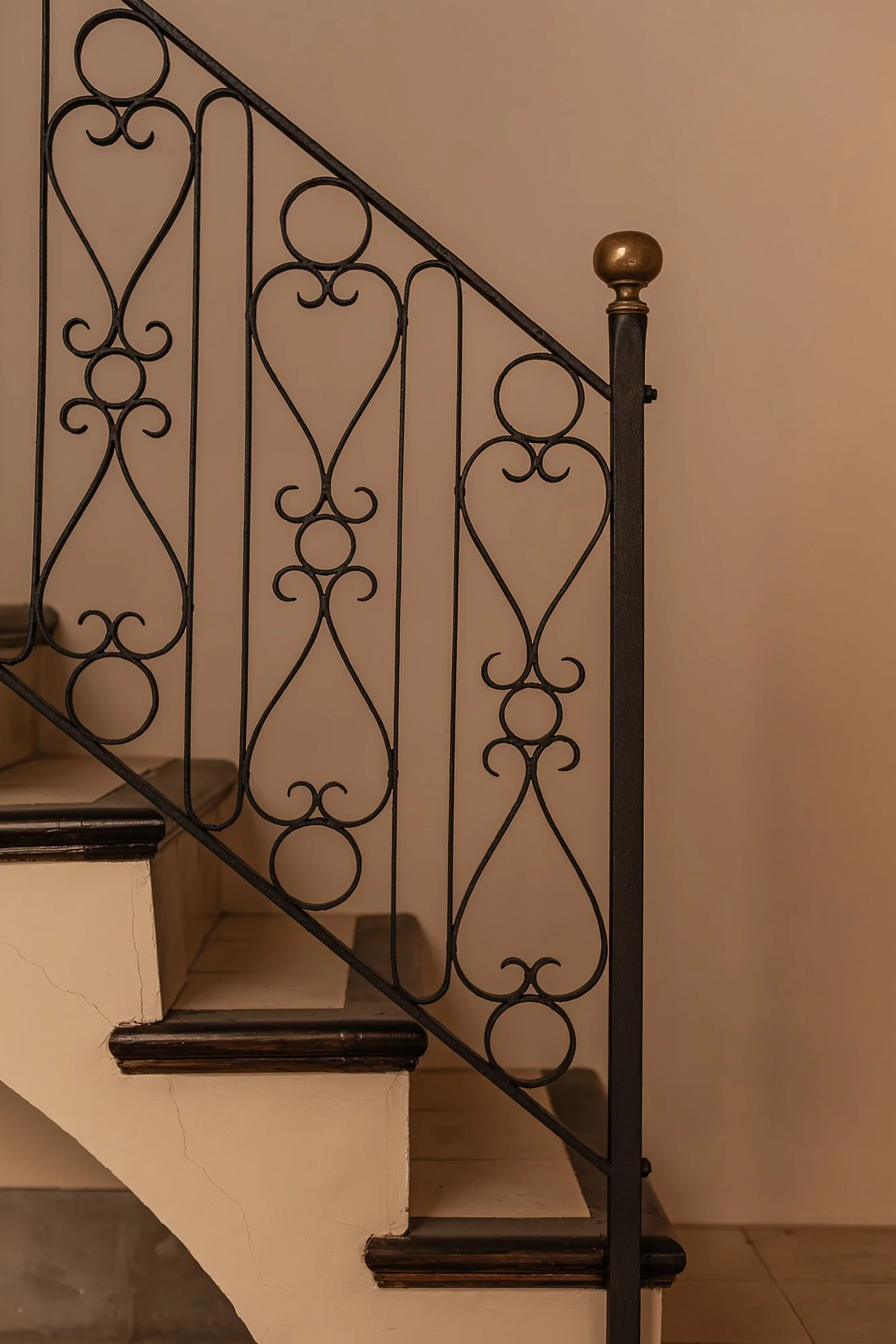 Interior staircase with ornate black wrought iron railing and beige walls.