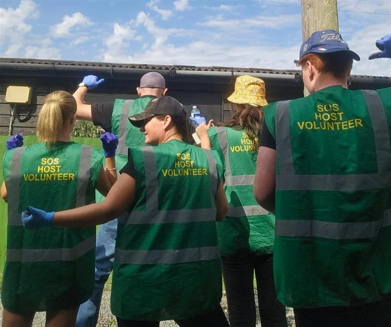 Group of volunteers wearing green vests labeled 'SOS Host Volunteer' working outdoors during the daytime.