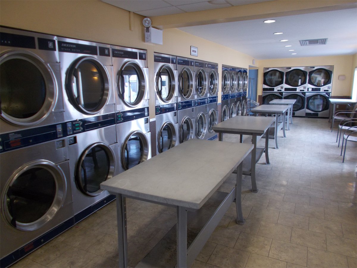 A laundromat with multiple stacked washers and dryers, tables, and chairs.