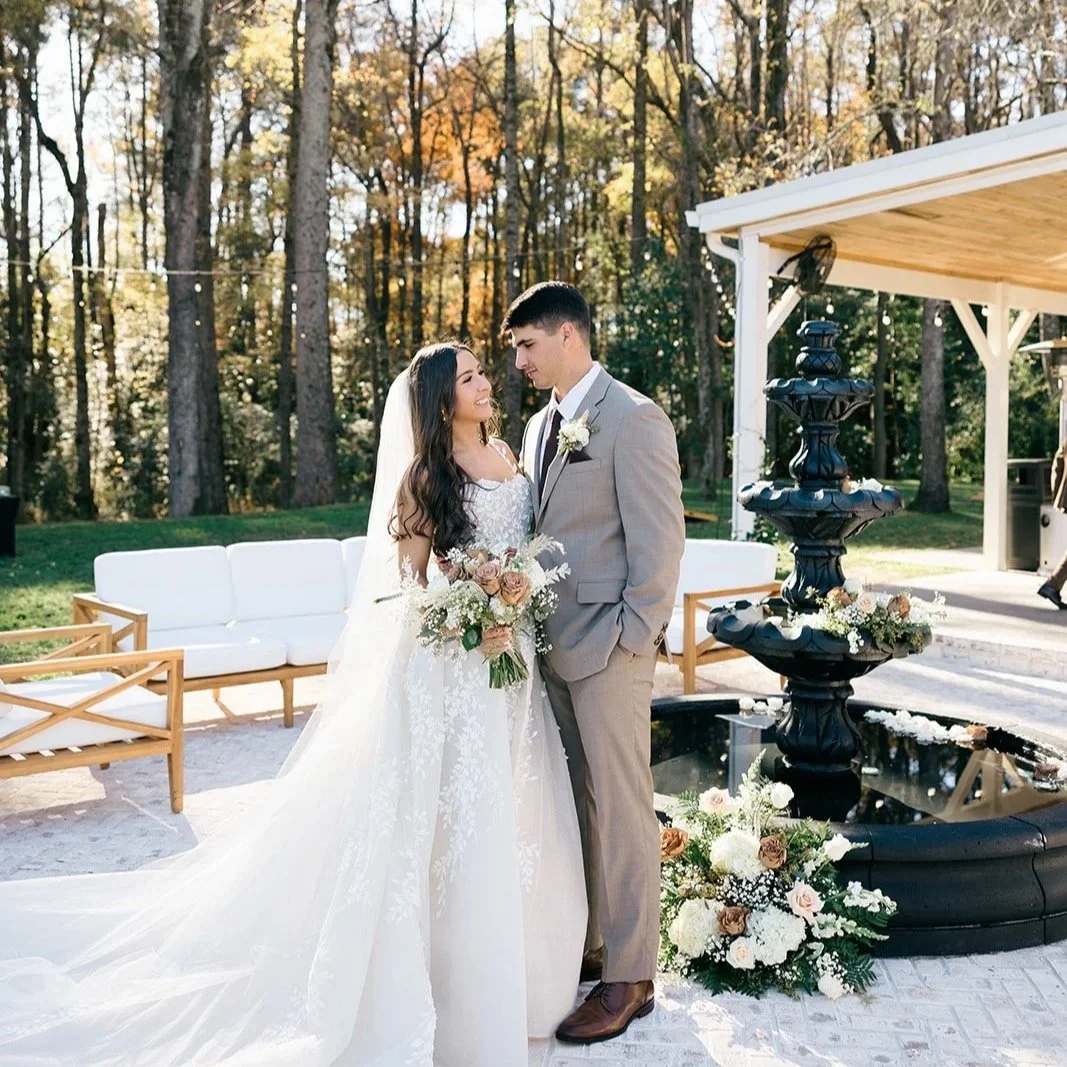 A bride and groom stand close together during their wedding, with a backdrop of trees and sunlight.