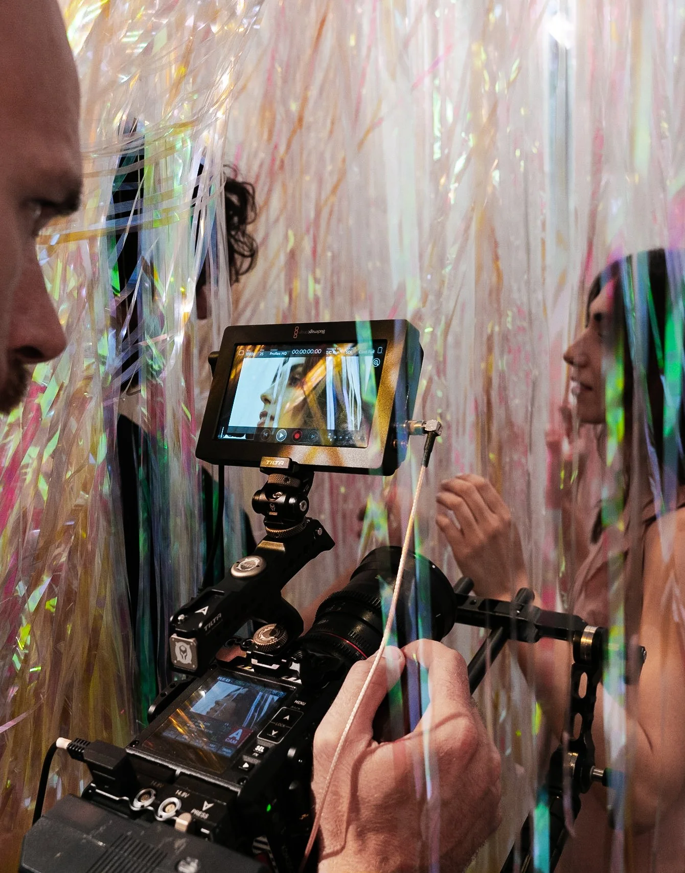 Un equipo de cine profesional grabando a una mujer con un fondo de tiras de plástico iridiscentes.
