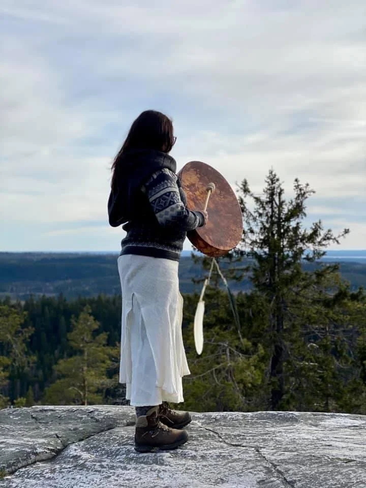 Nainen katsoo korkealle vuoren laella, jossa on metsä ja taivas taustalla, pitäen kultaista kannelta.