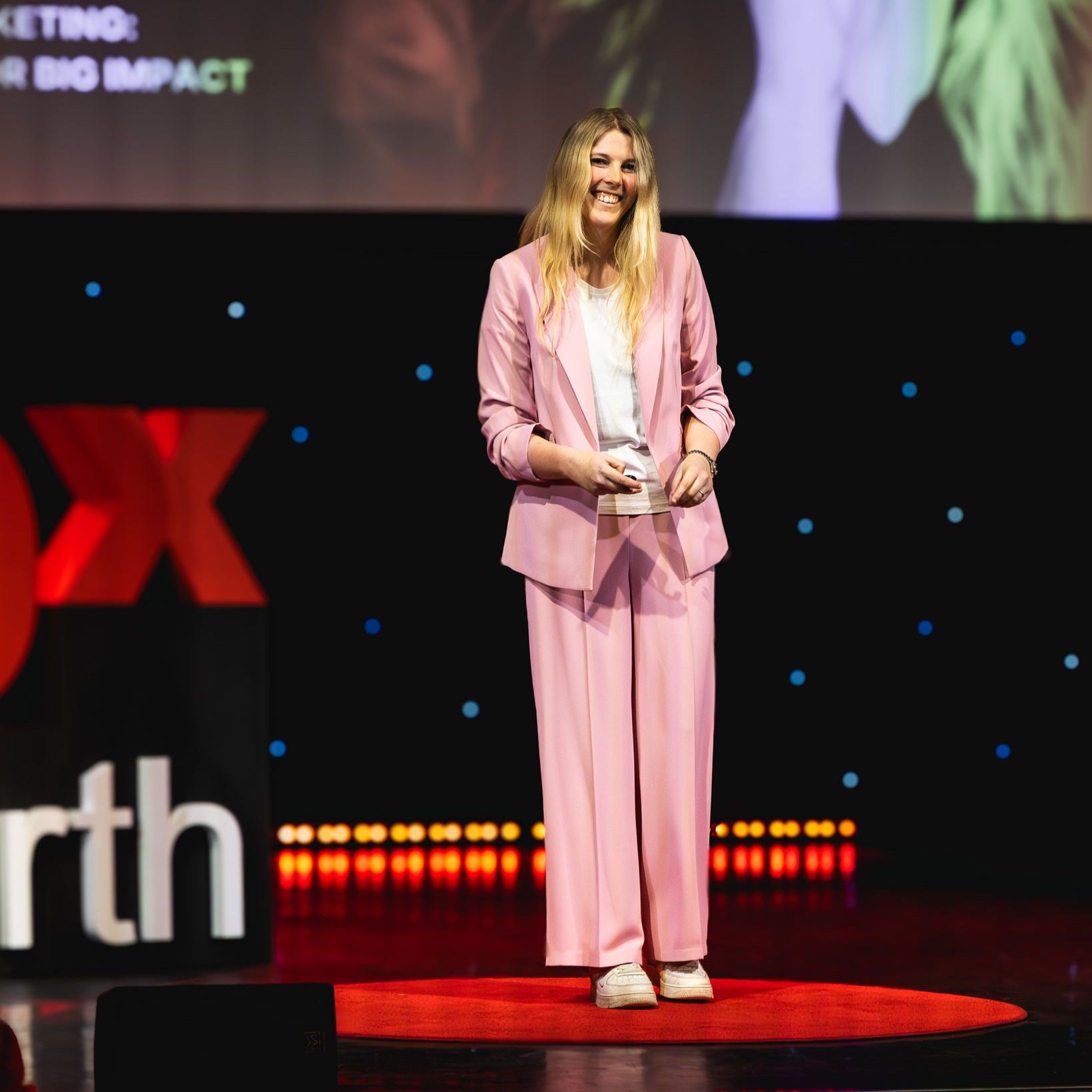 Woman in pink suit giving a presentation on stage at a TEDx event.