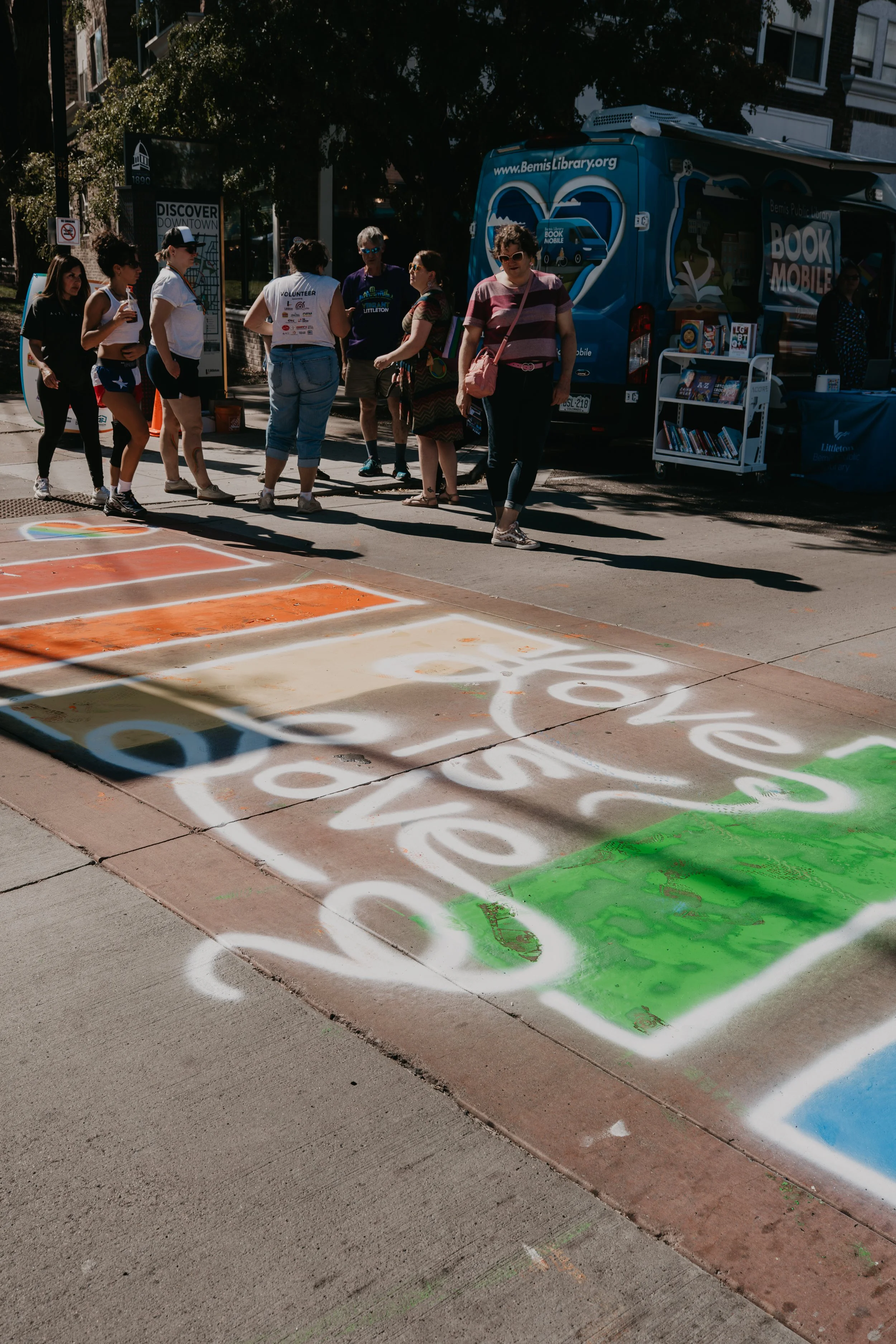 People gather beside the Bemis Public Library bookmobile on a downtown sidewalk, with books displayed on a mobile cart.