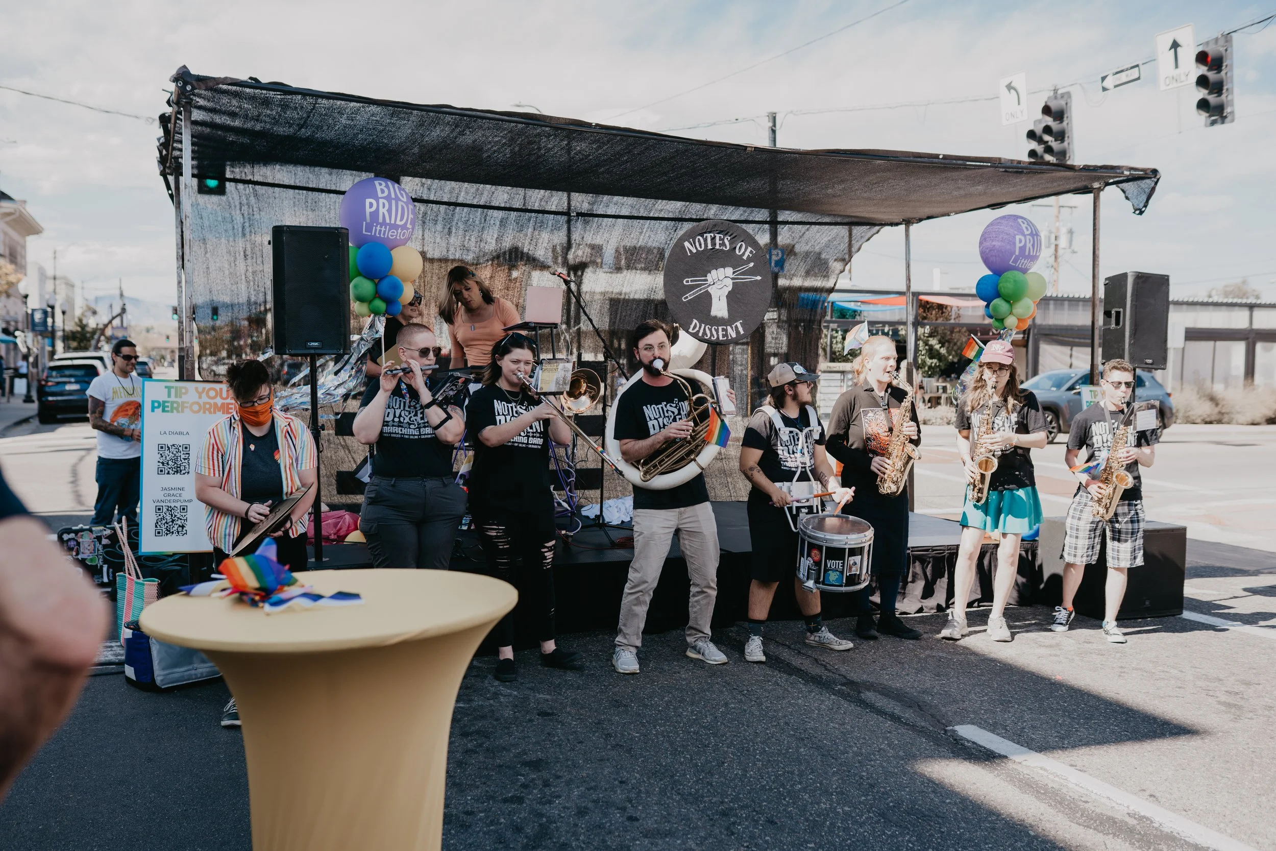 LGBTQ+ marching band performing at a Littleton Pride street festival with colorful balloons and rainbow flags